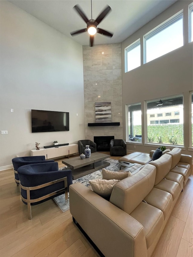 living room featuring a tiled fireplace, a healthy amount of sunlight, a high ceiling, and wood finished floors