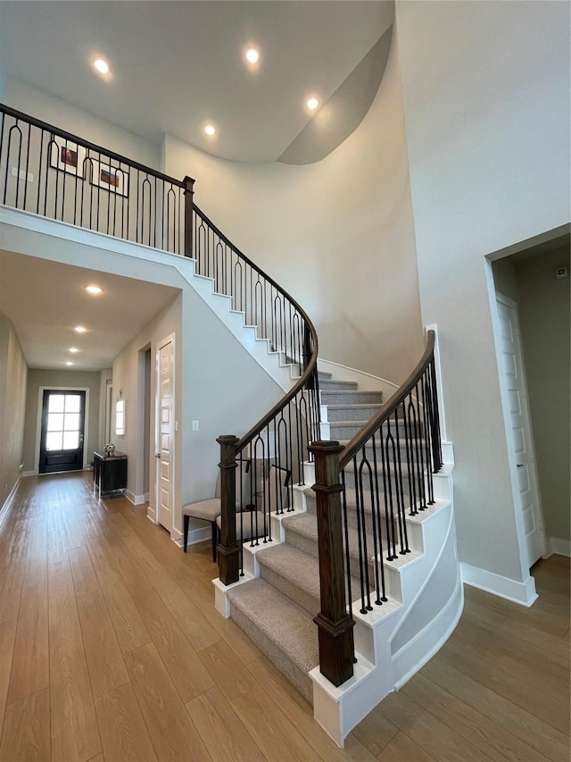 stairway featuring baseboards, wood finished floors, and a towering ceiling