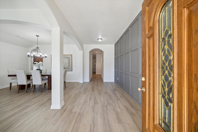 entrance foyer with a chandelier, light wood-style flooring, arched walkways, and baseboards