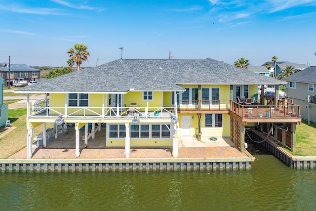 rear view of house featuring a patio area, a shingled roof, and a water view