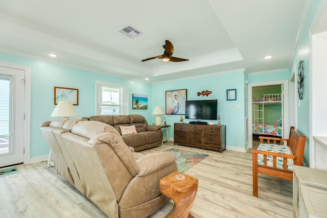 living room featuring a ceiling fan, visible vents, ornamental molding, light wood-style floors, and a raised ceiling