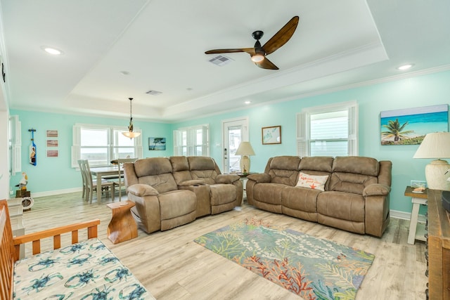 living area featuring a wealth of natural light, visible vents, a raised ceiling, and a ceiling fan