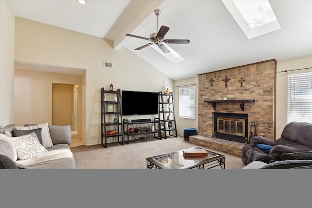 carpeted living room with visible vents, beam ceiling, a skylight, a fireplace, and ceiling fan