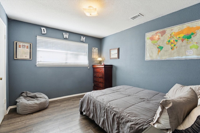 bedroom with visible vents, a textured ceiling, baseboards, and wood finished floors