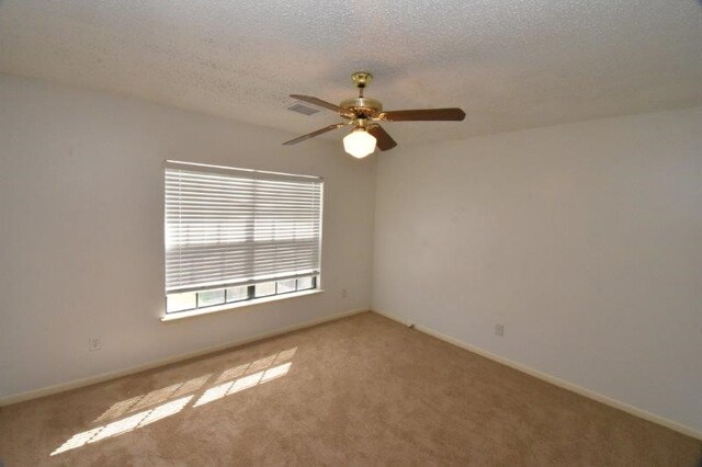 carpeted empty room with visible vents, a ceiling fan, baseboards, and a textured ceiling