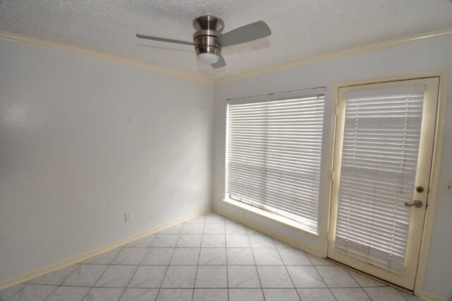 spare room with a textured ceiling, crown molding, light tile patterned floors, baseboards, and ceiling fan