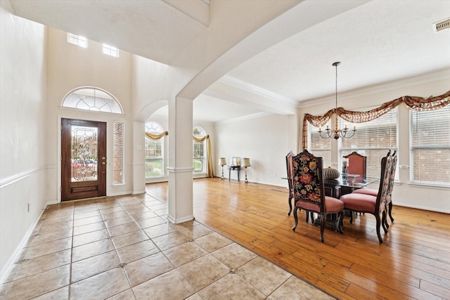 foyer with arched walkways, an inviting chandelier, crown molding, and light wood-style floors