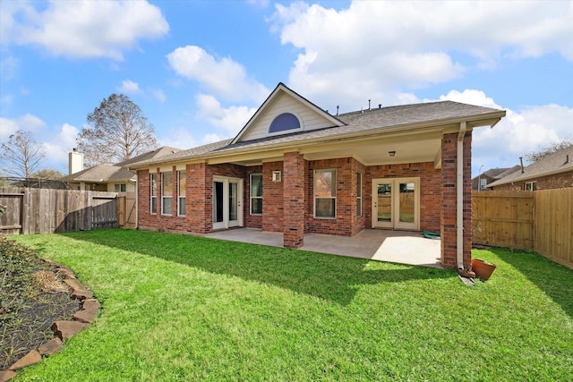 back of house with french doors, brick siding, a fenced backyard, and a lawn