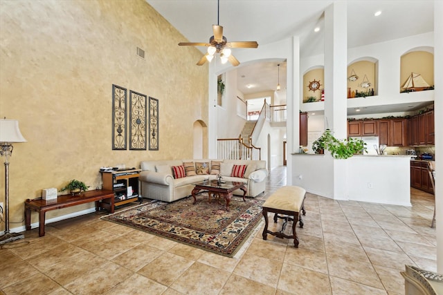 living area featuring visible vents, stairs, light tile patterned floors, a high ceiling, and a ceiling fan