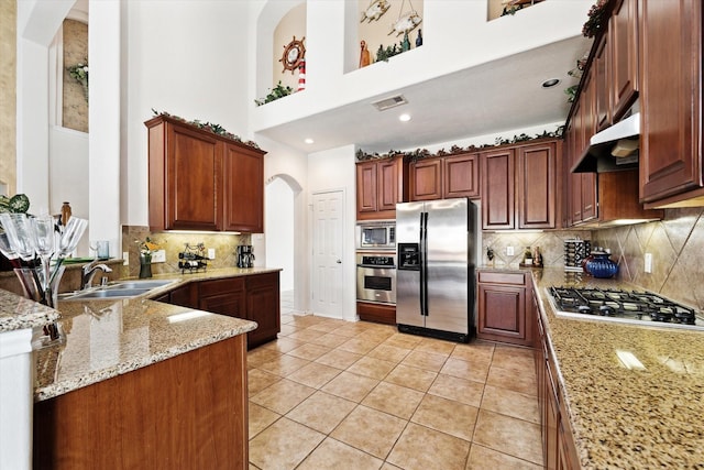 kitchen with under cabinet range hood, a sink, appliances with stainless steel finishes, light tile patterned flooring, and light stone countertops