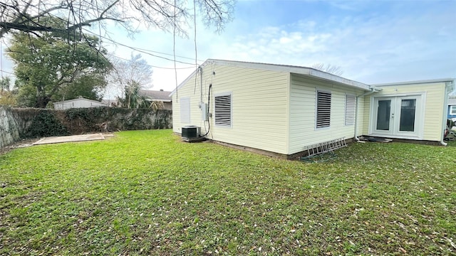 view of property exterior with central AC, french doors, a lawn, and a fenced backyard