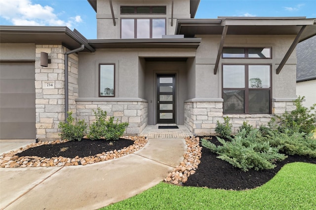 view of exterior entry featuring stone siding, stucco siding, and a garage