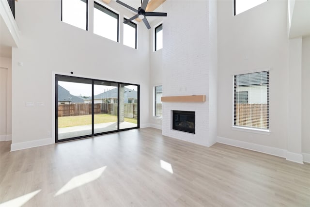 unfurnished living room with a ceiling fan, wood finished floors, baseboards, and a large fireplace