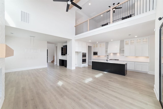 unfurnished living room featuring a ceiling fan, visible vents, baseboards, light wood-style flooring, and a towering ceiling