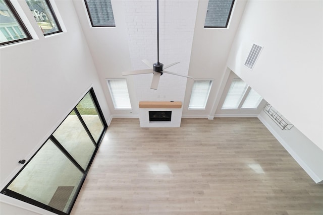 unfurnished living room featuring ceiling fan, light wood-style floors, a towering ceiling, and a fireplace