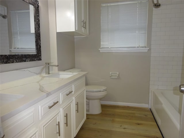 bathroom featuring wood finished floors, baseboards, double vanity, a sink, and toilet