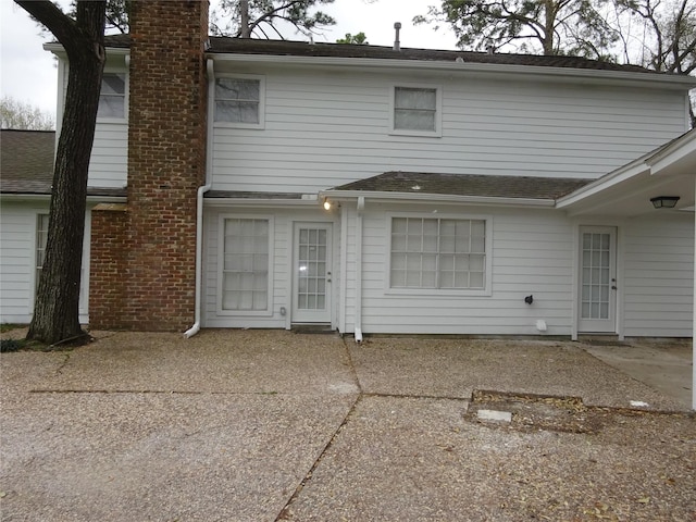 rear view of house featuring a chimney, a patio, and a shingled roof