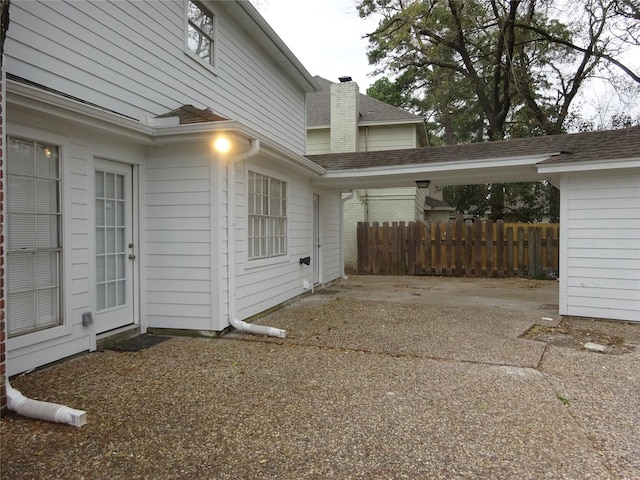 view of home's exterior featuring a carport, fence, driveway, and a chimney