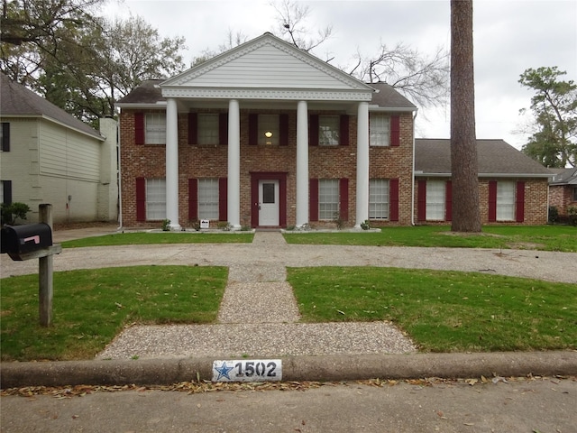 greek revival inspired property featuring a front yard, brick siding, and driveway