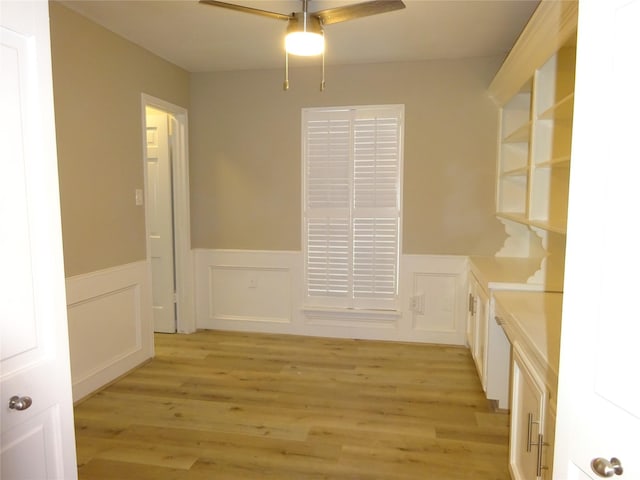 unfurnished dining area with light wood-style floors, ceiling fan, and wainscoting