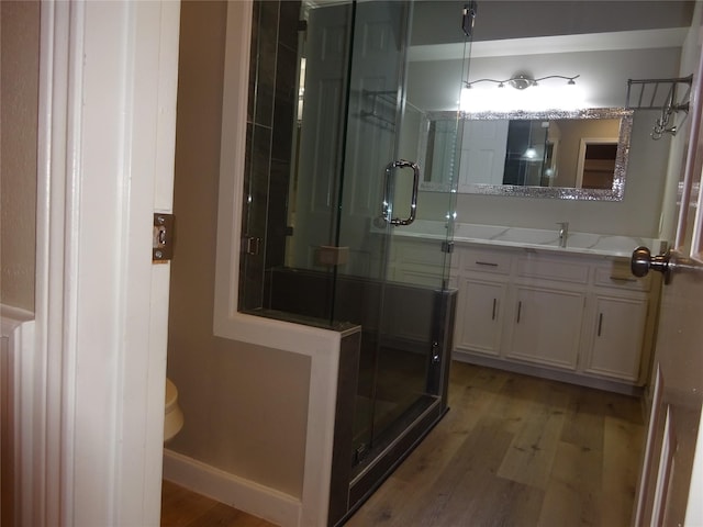 bathroom with baseboards, toilet, a stall shower, wood finished floors, and vanity