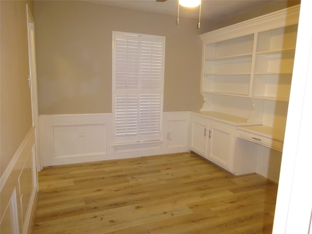 interior space with a ceiling fan, a wainscoted wall, and light wood finished floors