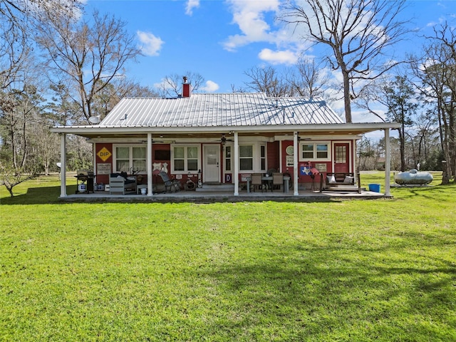 rear view of property featuring a ceiling fan, a lawn, a chimney, and metal roof