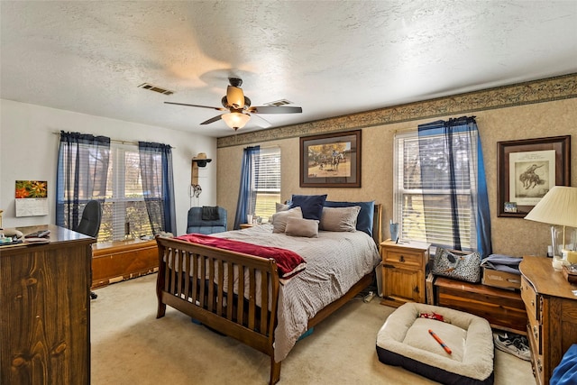 bedroom featuring a ceiling fan, light colored carpet, visible vents, and a textured ceiling