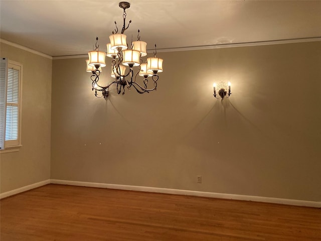 unfurnished room featuring a chandelier, crown molding, baseboards, and wood finished floors