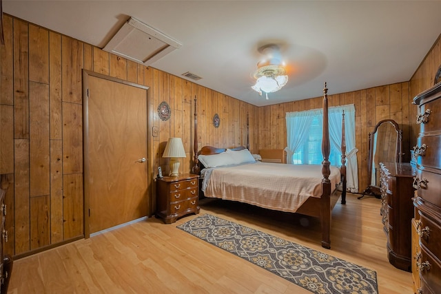 bedroom with light wood-type flooring, visible vents, wooden walls, and a ceiling fan