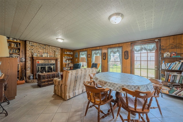 dining area with light tile patterned floors, built in features, wooden walls, and a brick fireplace