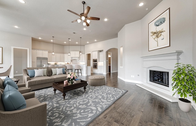 living area featuring recessed lighting, arched walkways, dark wood-type flooring, and a fireplace with raised hearth