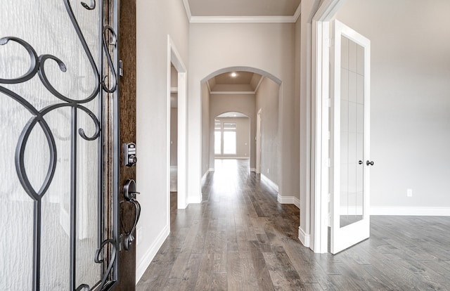 entryway featuring arched walkways, crown molding, dark wood-type flooring, and baseboards