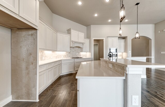 kitchen featuring a center island with sink, dark wood finished floors, light countertops, appliances with stainless steel finishes, and backsplash