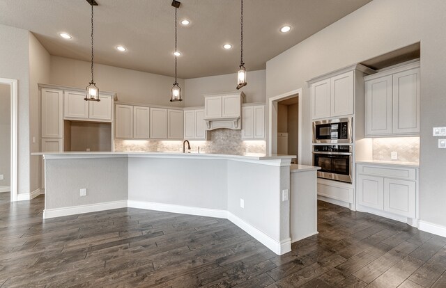 kitchen with dark wood finished floors, a large island, light countertops, appliances with stainless steel finishes, and hanging light fixtures