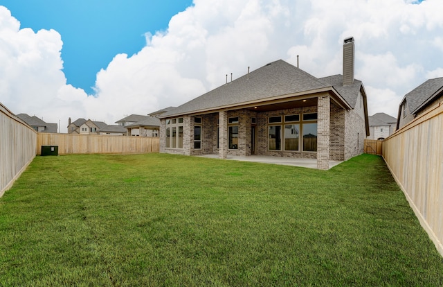 back of property featuring brick siding, a chimney, a fenced backyard, a yard, and a patio