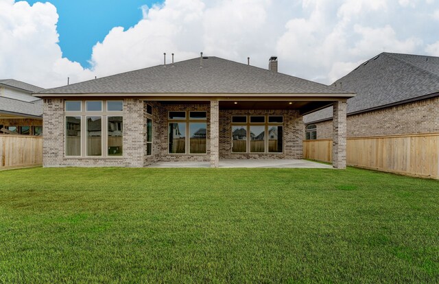 rear view of house with a patio, a fenced backyard, a chimney, a lawn, and brick siding