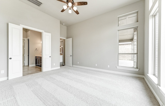 unfurnished bedroom featuring baseboards, visible vents, ceiling fan, ensuite bathroom, and light carpet