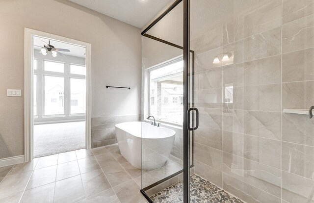 bathroom with ceiling fan, a freestanding bath, a stall shower, tile patterned floors, and tile walls