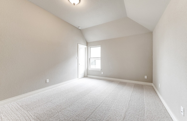 spare room with light colored carpet, baseboards, and vaulted ceiling