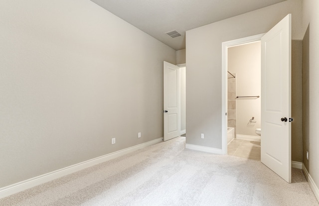 unfurnished bedroom with light colored carpet, visible vents, ensuite bathroom, and baseboards