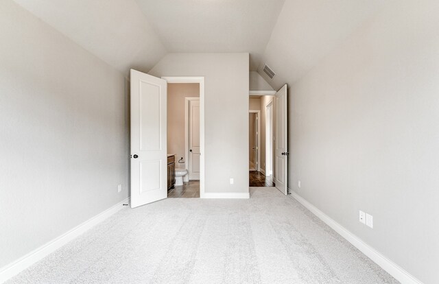 unfurnished bedroom featuring light carpet, visible vents, baseboards, and lofted ceiling