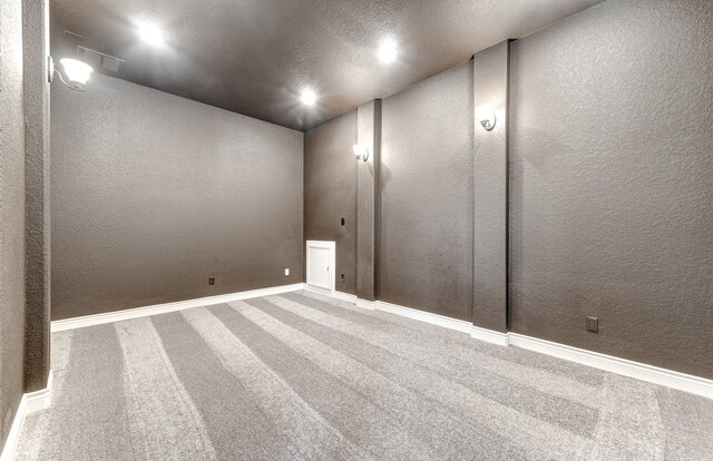 spare room featuring carpet, visible vents, baseboards, a textured ceiling, and a textured wall