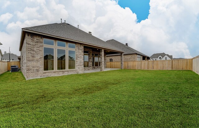 back of property with central air condition unit, brick siding, a fenced backyard, and a yard