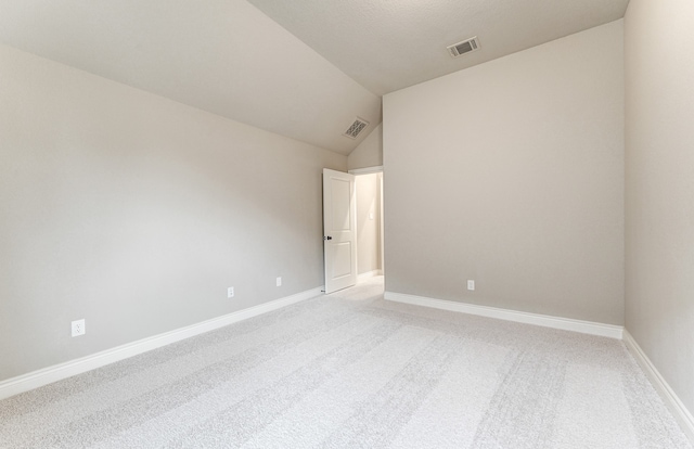 spare room with visible vents, baseboards, light colored carpet, and vaulted ceiling