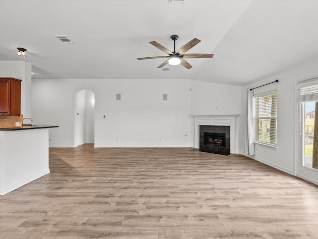 unfurnished living room featuring visible vents, arched walkways, a high end fireplace, a sink, and light wood-style floors