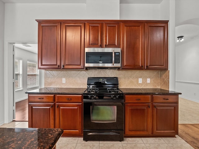 kitchen with stainless steel microwave, arched walkways, black range with gas stovetop, and decorative backsplash