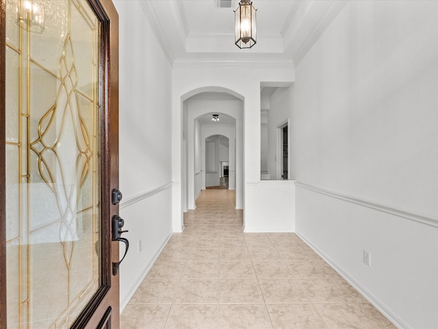 hallway featuring light tile patterned floors, visible vents, arched walkways, ornamental molding, and a raised ceiling