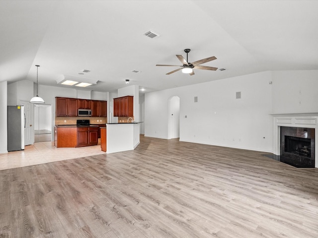 unfurnished living room featuring visible vents, light wood-style flooring, a premium fireplace, lofted ceiling, and ceiling fan