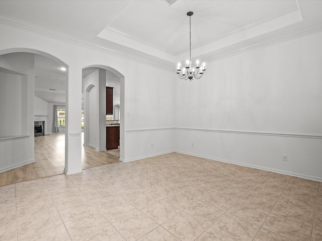 empty room with crown molding, baseboards, a tray ceiling, a fireplace, and light tile patterned flooring